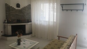 A living room with a fireplace, a sofa, a coffee table with a floral vase, and a window with sheer curtains. - Calista Luxury Appt (Kassandra)