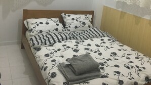 A single bed with a floral-patterned bedspread, two pillows with a black and white design, and a folded grey towel on the bed. - Calista Luxury Appt (Kassandra)