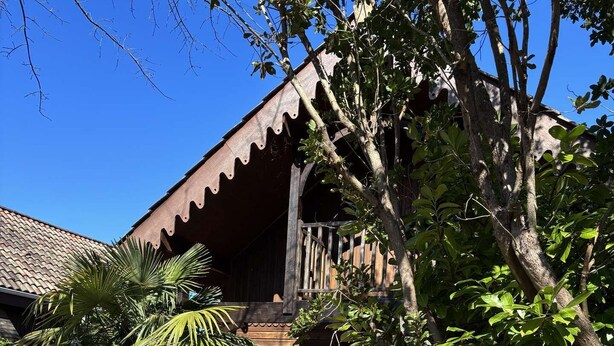 A wooden house with a balcony, surrounded by trees and a wooden fence.