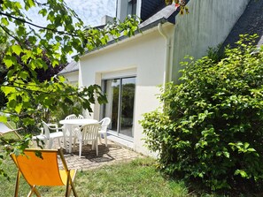 A patio with a table and chairs, a sliding glass door, and a hedge.