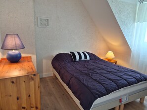 A bedroom with a bed, two bedside lamps, a wooden nightstand, and a small wall decoration.