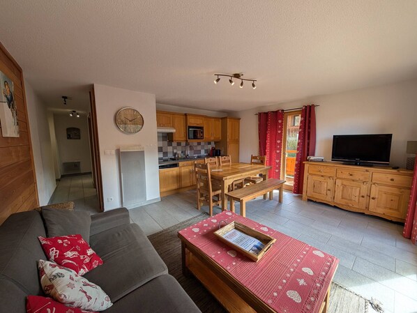 Ein gemütliches Wohnzimmer mit einer Couch, einem Holzesstisch und einer Küche im Hintergrund.