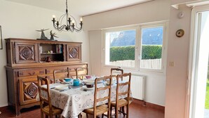 A dining area with a table set for four, surrounded by wooden chairs. A wooden cabinet with decorative patterns is to the left.