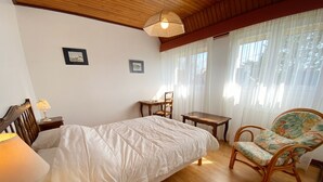 A bedroom with a bed, a chair, a table, and a lamp.