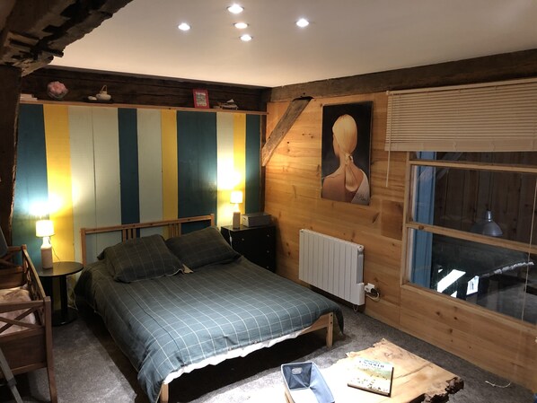 A cozy bedroom with a bed, bedside tables, a lamp, a radiator, and a window with blinds.