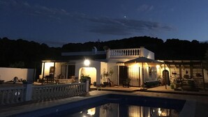 Een modern huis met een zwembad, een overdekt terras en uitzicht op de omliggende heuvels.