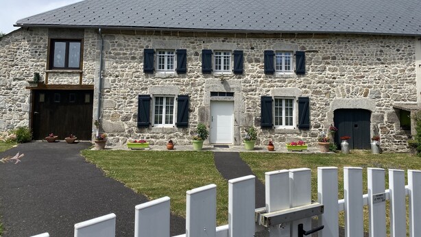 Ein Steinhaus mit einem zentralen Eingang, zahlreichen Fenstern mit Fensterläden und einem gepflasterten Zugang.
