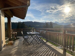 A wooden deck with a table and chairs, overlooking a mountainous landscape.