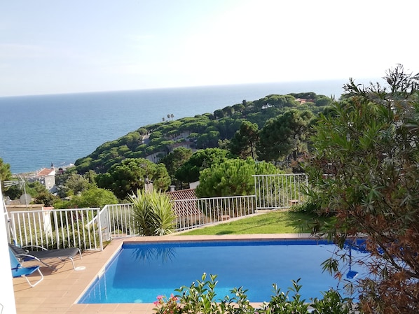 Una piscina con vistas al mar y una colina con árboles.