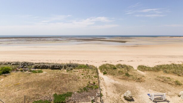 A beach with a sandy path leading to a bench and a gate.