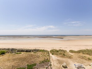 A beach with a sandy path leading to a bench and a gate.