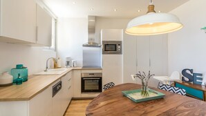A modern kitchen with white cabinets, a wooden countertop, a built-in oven, a microwave, and a hanging pendant light.