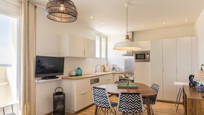 A modern kitchen with a dining area, featuring a flat-screen TV, a microwave, and a wooden dining table with black and white patterned chairs.