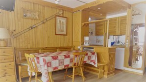 Una stanza accogliente con un tavolo da pranzo in legno, sedie, un angolo cottura e un letto.