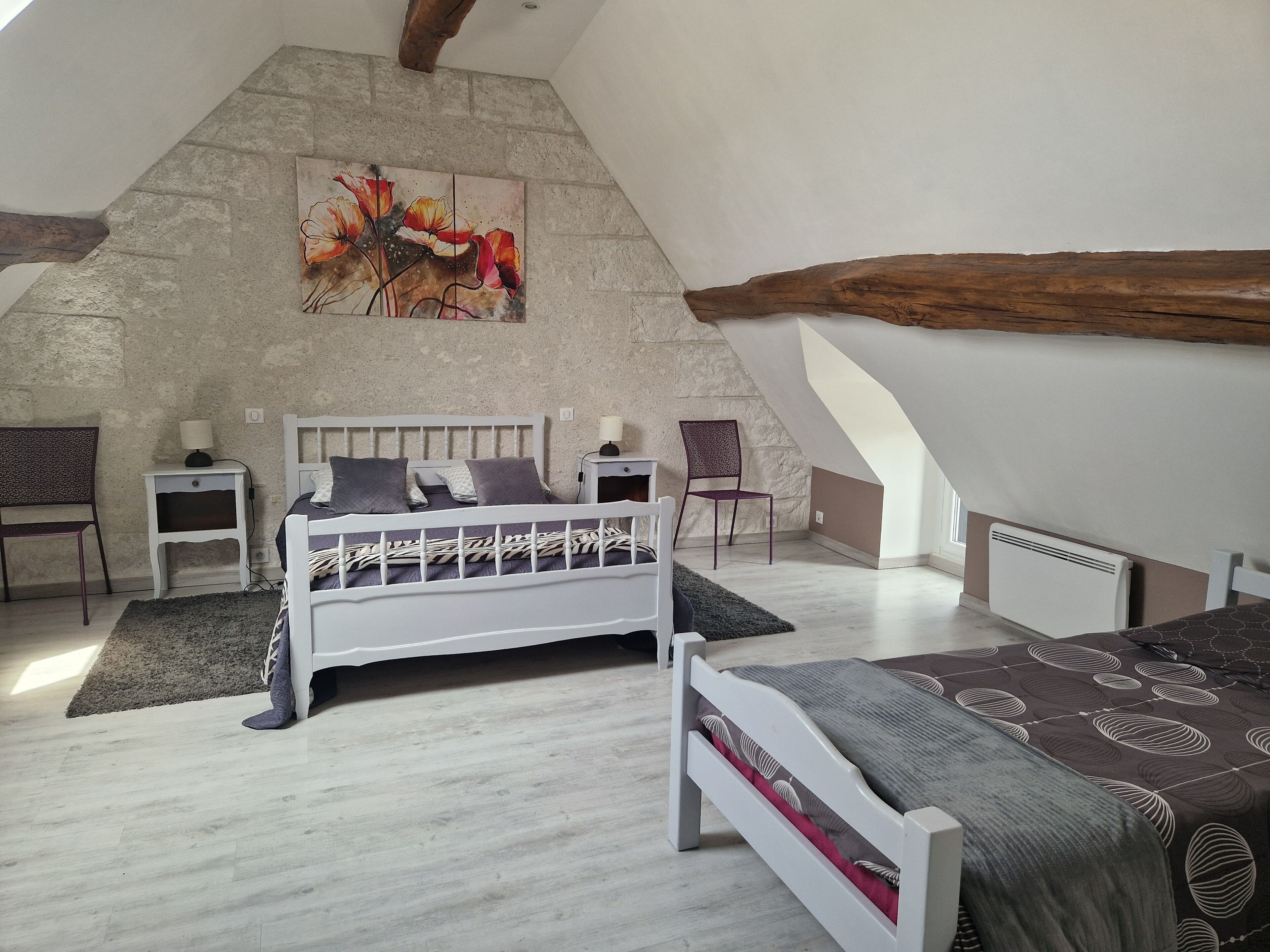 A bedroom with a sloped ceiling, a bed, a chair, a nightstand, and a painting on the wall.