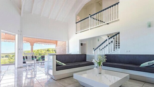 A spacious living area with a modern design, featuring a large sofa, a coffee table, and a staircase leading to an upper level. - VILLA BETWEEN SEA AND MOUNTAIN  (Pointe noire)