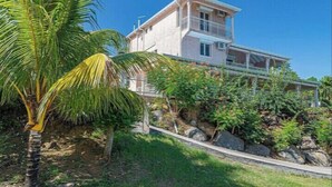 A two-story house with a balcony, surrounded by tropical vegetation and rocks. - VILLA BETWEEN SEA AND MOUNTAIN  (Pointe noire)