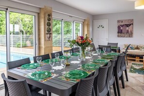 Un coin repas avec une table dressée pour six personnes, de grandes fenêtres et une vue sur une piscine.