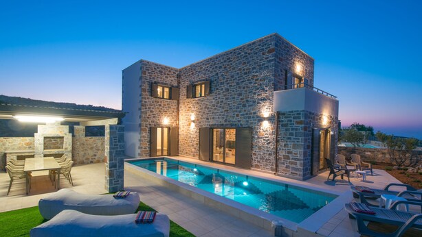 Une maison moderne dotée d’une piscine, d’une façade en pierre et d’un espace extérieur aménagé pour se détendre.