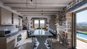 Une cuisine moderne dotée d’un grand îlot central, de murs en pierre et offrant une vue sur les montagnes.