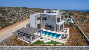 Un bâtiment moderne en pierre, doté d’une piscine, d’un espace extérieur aménagé et offrant une vue sur le paysage environnant.