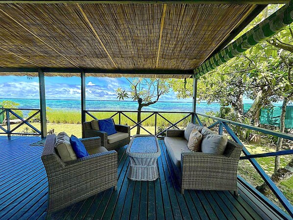 A covered outdoor seating area with wicker furniture and a view of the ocean.