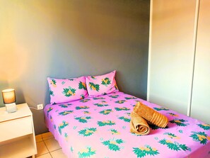 A single bed with a floral bedspread, a rolled towel, a bedside table with a lamp, and a wardrobe.