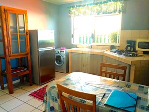 A kitchen with a refrigerator, washing machine, and a dining area with a table and chairs.