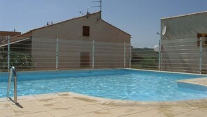 A swimming pool with a tiled deck, surrounded by a metal fence, and adjacent to a building with a sloped roof. - Studio mezzanine with pool, parking, Narbonne-Plage (Narbonne-Narbonne Plage-Narbonne Plage)