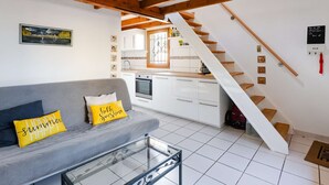 A modern apartment with a grey sofa, a glass coffee table, a kitchen with white cabinets, and a wooden staircase. - Studio mezzanine with pool, parking, Narbonne-Plage (Narbonne-Narbonne Plage-Narbonne Plage)