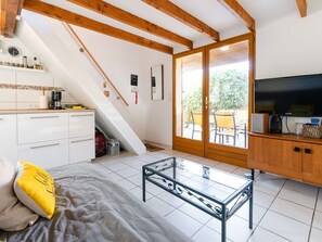 Um espaço compacto com cozinha compacta, mesa de vidro, cama com travesseiro amarelo, televisão e porta de correr que dá para área externa.