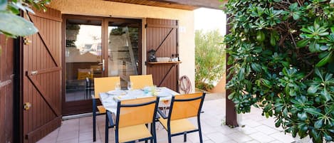An outdoor patio with a table set for two, surrounded by chairs, and a wooden pergola overhead.