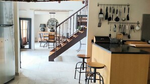 Una cocina con una isla central, taburetes de bar, un colgador para ollas y una escalera que sube a un nivel superior.