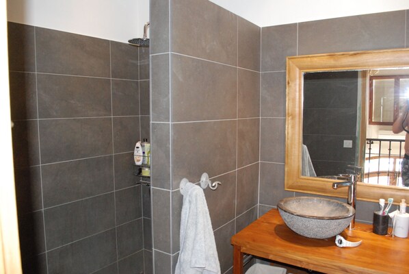 Un baño con baldosas oscuras, un mueble de tocador de madera, un espejo grande y un perchero para toallas.