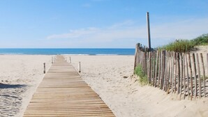 Un paseo marítimo de madera que conduce a una playa arenosa bajo un cielo azul despejado.