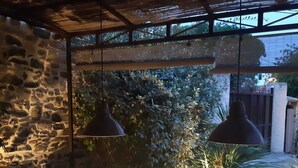 Un área de comedor al aire libre con pared de piedra y lámparas colgantes.