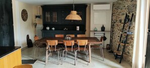 Un coin repas avec une table et des chaises en bois, un buffet en bois foncé doté de portes en verre, et un mur en pierre avec des étagères.