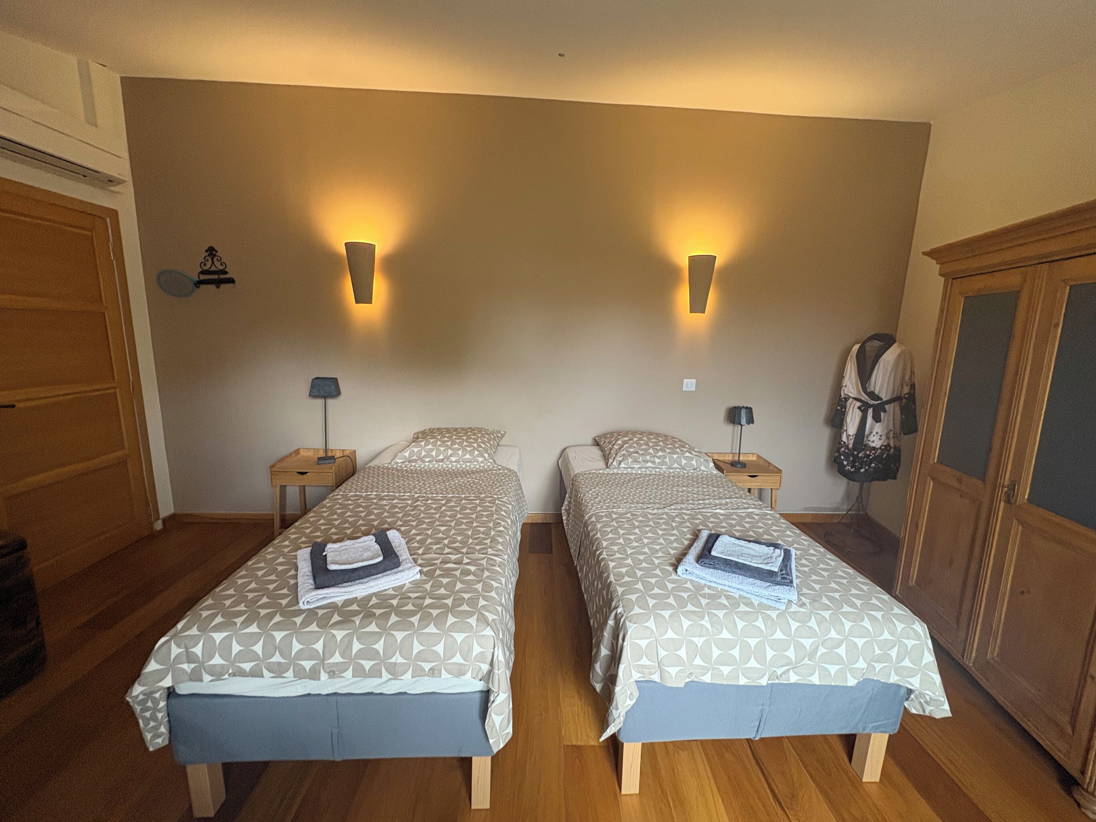 Habitación con dos camas, cada una con colcha y almohadas estampadas, dos mesitas de noche con lámparas, un armario y un estante en la pared con un objeto decorativo.