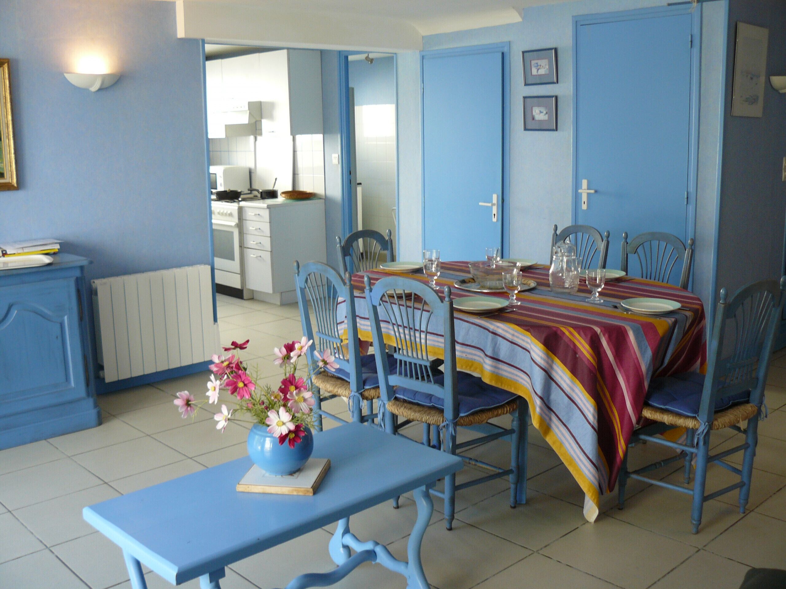 Un comedor con una mesa dispuesta para cuatro, sillas azules y un jarrón de flores sobre una mesa azul.