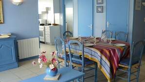 A dining area with a table set for four, blue chairs, and a vase of flowers on a blue table. - TRIDILLE 1 - Apartment for rent with garden in Carnac - D6 (Carnac)