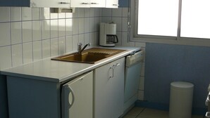 A compact kitchen with white cabinets, a sink, a coffee maker, and a window. - TRIDILLE 1 - Apartment for rent with garden in Carnac - D6 (Carnac)