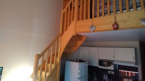 Een houten trap die leidt naar een hoger gelegen ruimte met een keuken eronder.