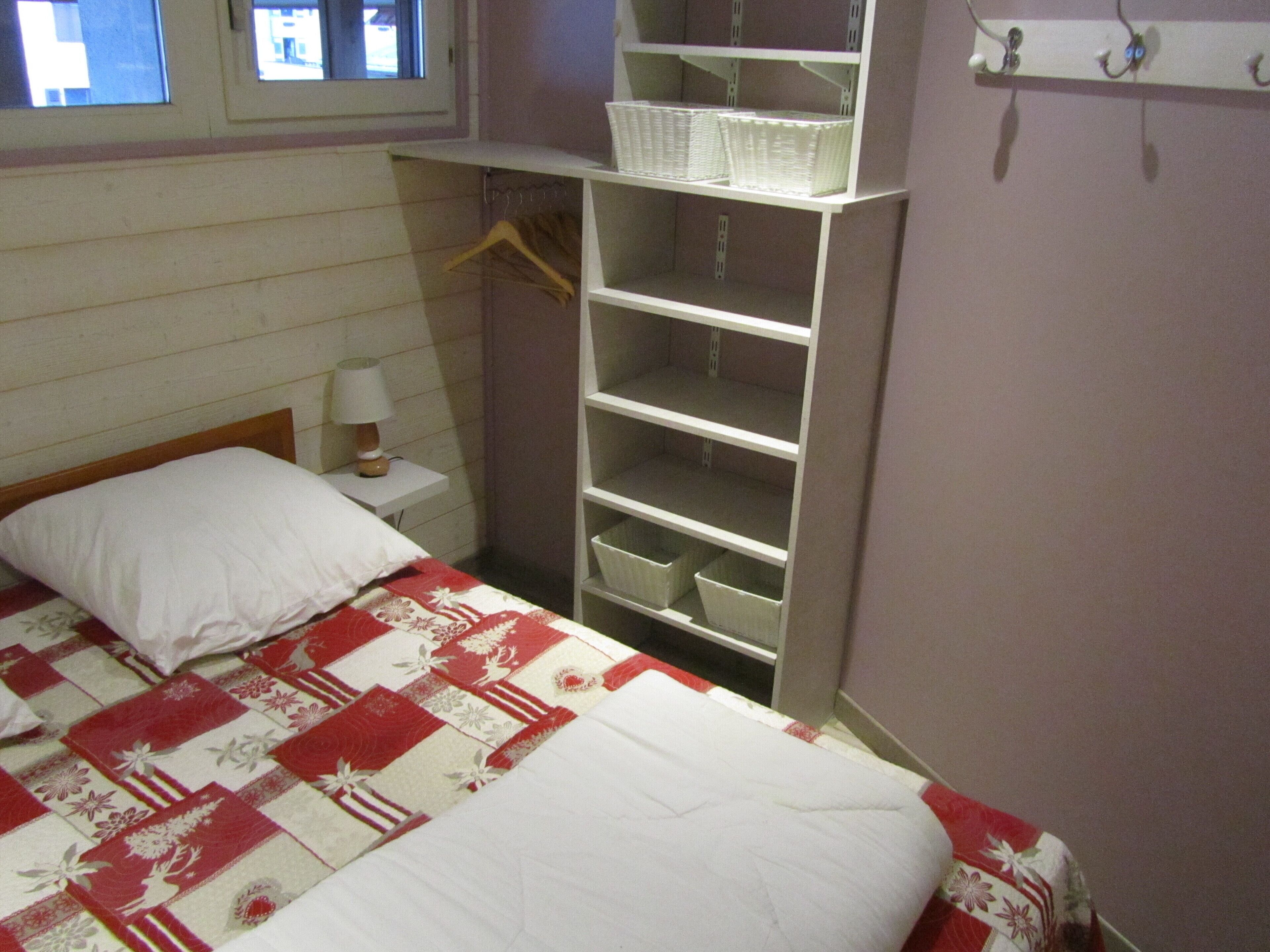 Une chambre à coucher avec un lit, une table de chevet, une étagère avec des paniers et une fenêtre.