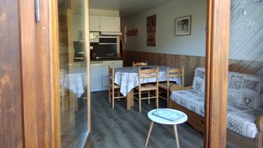 Een knus woongedeelte met een eettafel, stoelen, een klein rond tafeltje, een bank en een kitchenette.