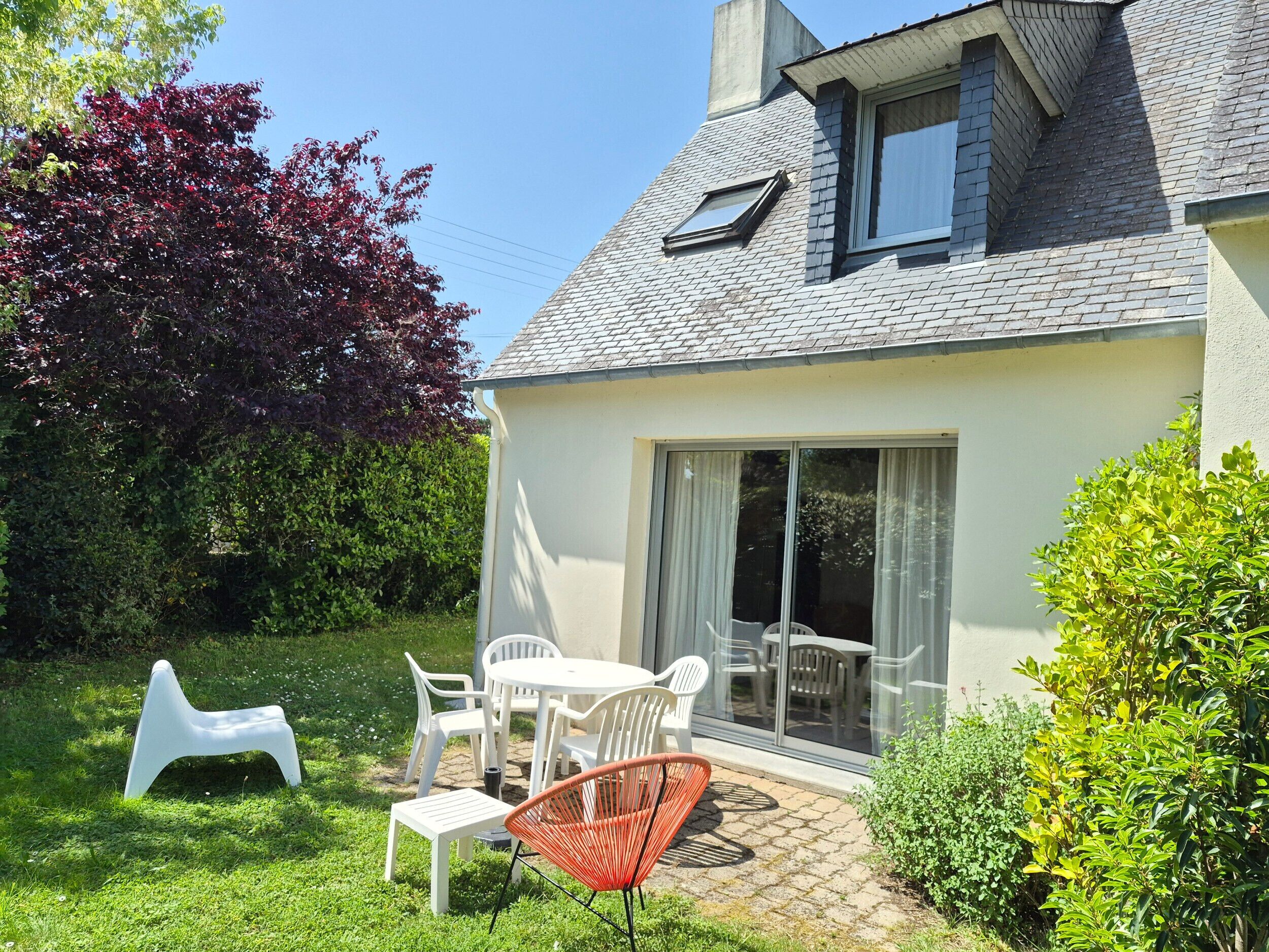 A house with a patio, a dining table with chairs, a white chair, and a red chair.
