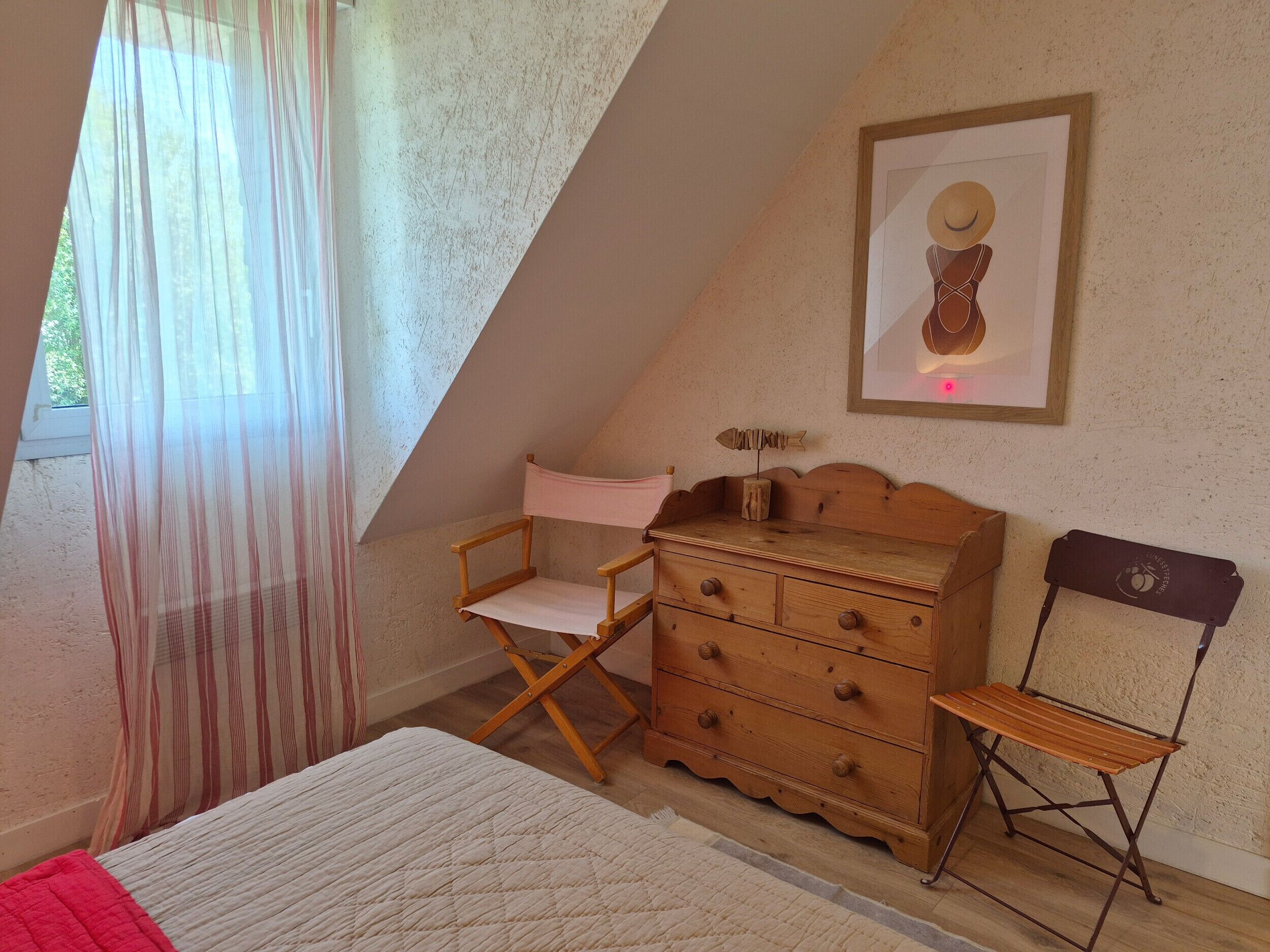Ein Schlafzimmer mit einem Bett, einer Holzkommode, einem Regiestuhl und einem gerahmten Bild an der Wand.