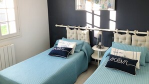 Una camera da letto con due letti, entrambi con biancheria e cuscini blu abbinati, una testiera bianca, un comodino con una lampada e una finestra con persiane.
