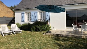 Una casa con patio, sedie bianche, un ombrellone azzurro e un tetto in mattoni.