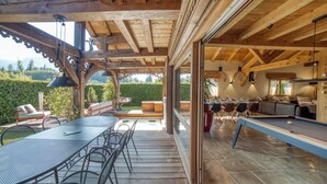 A wooden deck with a pool table, outdoor seating, and a view of a lush garden.