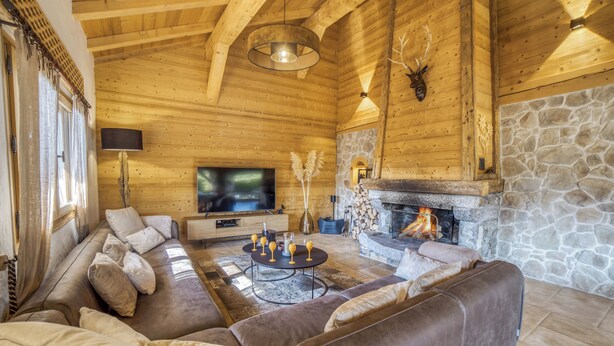 A cozy log cabin interior with a stone fireplace, leather sofas, and a flat-screen TV.